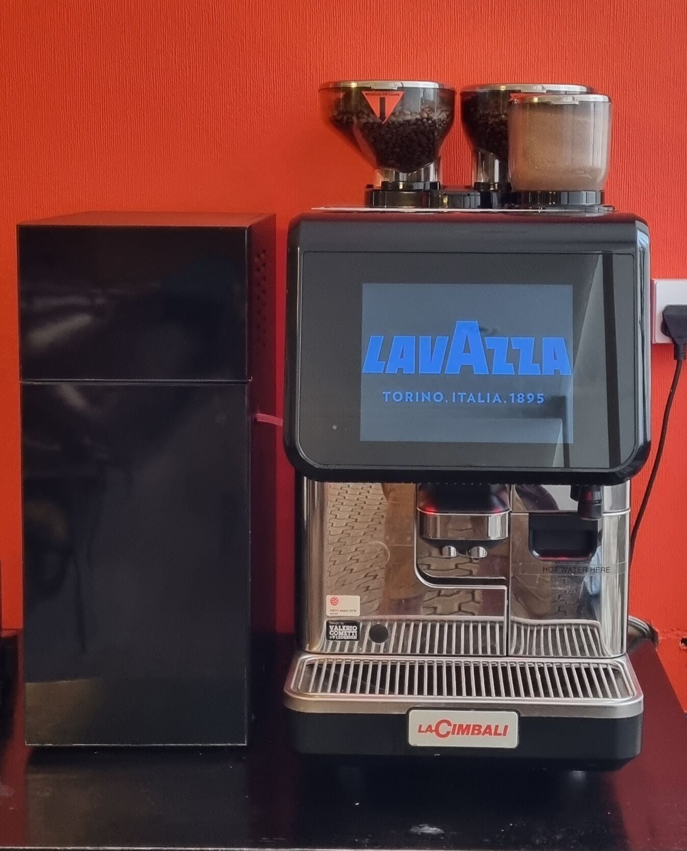 A La Cimbali espresso machine with a digital display, placed against a red background.