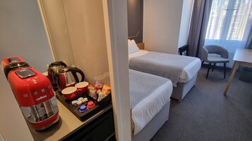 Ein Hotelzimmer mit Küchenzeile, zwei Betten, einem Sessel und Blick auf die Stadt durch das Fenster.