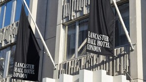 The exterior of Lancaster Hall Hotel in London, featuring a modern facade with large windows and black flags hanging from the building. - Lancaster Hall Hotel (London)