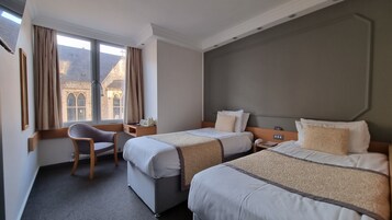 Een hotelkamer met twee bedden, een bureau, een stoel en een groot raam met gordijnen.