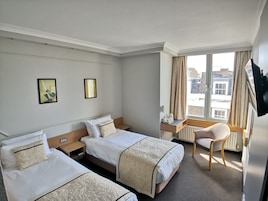 Ein Hotelzimmer mit zwei Betten, einem Schreibtisch, einem Stuhl und einem großen Fenster mit Vorhängen.