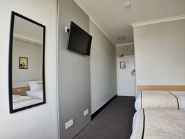 A hotel room with a bed, a television mounted on the wall, a door with a lock, and a small framed picture on the wall.