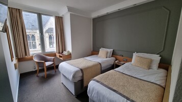 Ein Hotelzimmer mit zwei Betten, einem Schreibtisch, einem Stuhl und einem fenster mit Vorhängen.