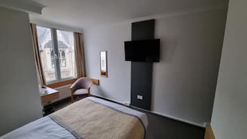 Habitación de hotel con cama, escritorio, silla, ventana y televisor de pantalla plana montado en la pared.