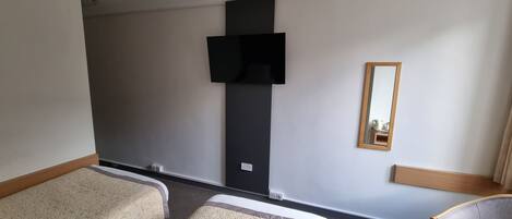 A hotel room with two single beds, a flat-screen TV mounted on the wall, and a mirror.