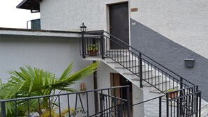 A building with a staircase leading to a door, a small balcony with a railing, and potted plants. - SUNNY VACATION APARTMENTS IN A QUIET LOCATION WITH A FANTASTIC LAKE VIEW (DUE COSSANI Luino Piemont)