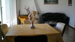 A dining area with a table covered in a yellow tablecloth, a vase with flowers, a black sofa, and a painting on the wall. - SUNNY VACATION APARTMENTS IN A QUIET LOCATION WITH A FANTASTIC LAKE VIEW (DUE COSSANI Luino Piemont)