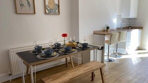 A modern dining area with a wooden table set for four, a bench, and a kitchen area with white cabinets and a countertop. - Beautiful Poole House 5 mins to Sandbanks +Netflix (Poole)