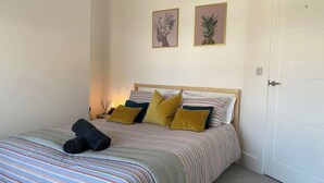 A bedroom with a bed, pillows, a nightstand, and two framed pictures on the wall. - Beautiful Poole House 5 mins to Sandbanks +Netflix (Poole)