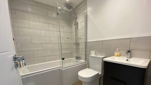 A modern bathroom with a glass-enclosed shower, a white toilet, a sink with a black cabinet, and a wooden floor. - Beautiful Poole House 5 mins to Sandbanks +Netflix (Poole)