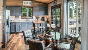 Une cuisine moderne avec des meubles de couleur sombre, une table à manger en verre et une vue sur l’extérieur.