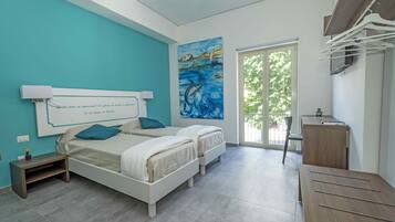 A bedroom with two beds, a desk, a chair, a window, and a painting on the wall.