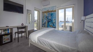 A bedroom with a bed, a desk, a chair, a TV, and a painting.