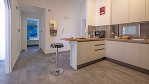 A modern kitchen with a central island, a microwave, and a coffee machine. There is a painting on the wall and a door leading to another room.