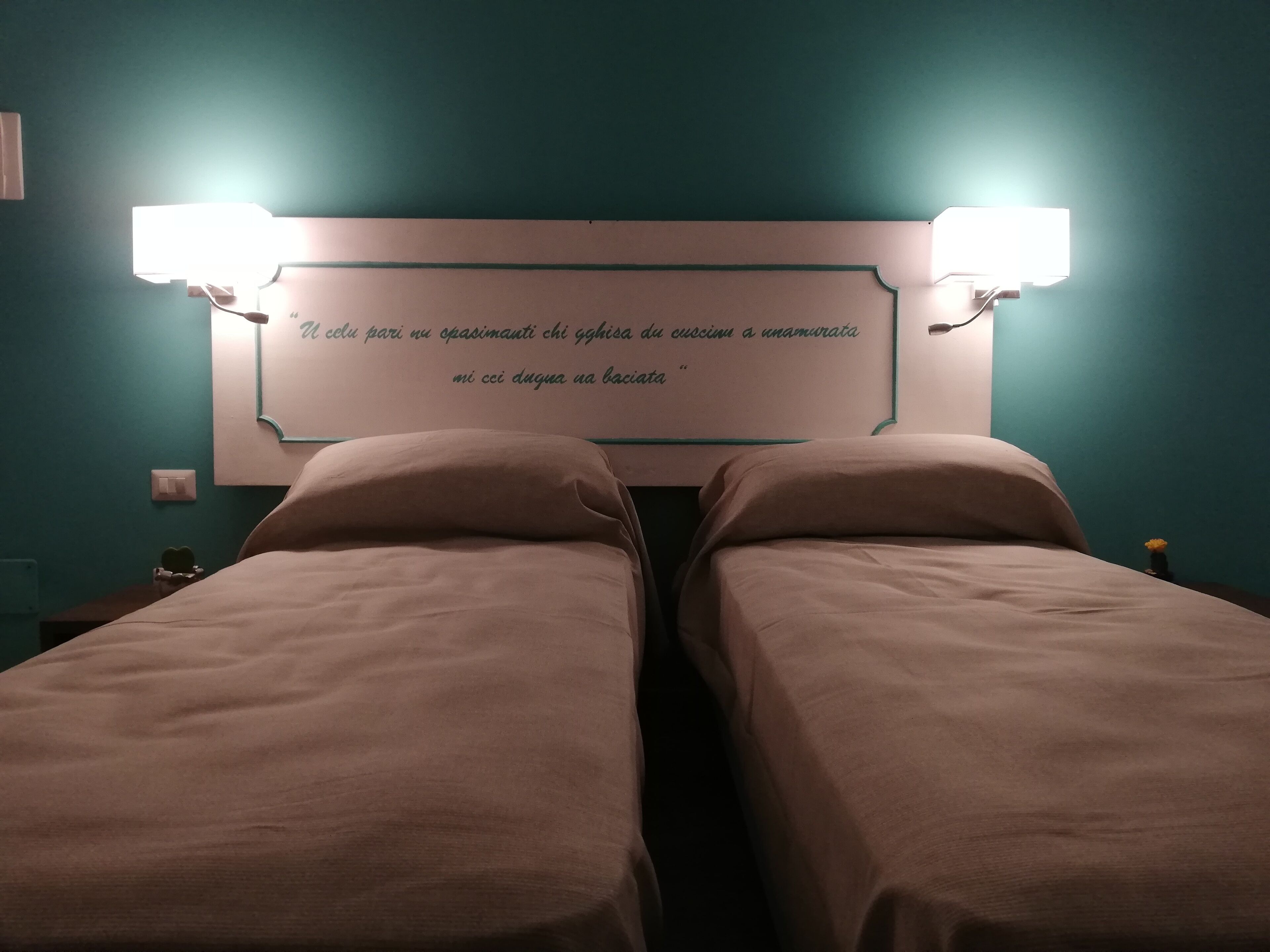 Ein Hotelzimmer mit zwei Einzelbetten, einer Wandleuchte und einer dekorativen Wandplatte.