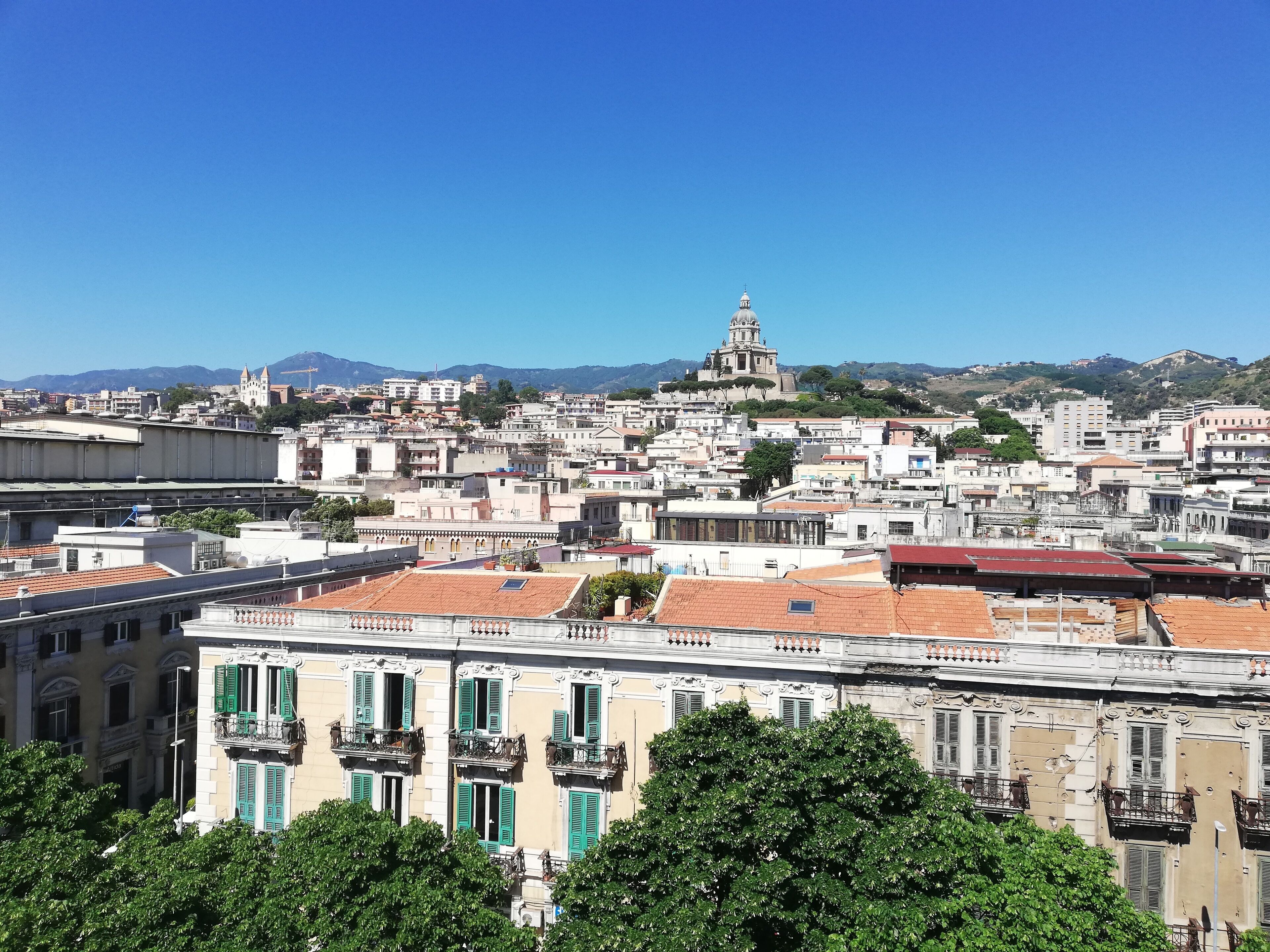 Paesaggio urbano con edifici storici, una chiesa importante con una cupola e montagne sullo sfondo.