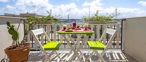 Un balcón con una mesa lista para dos personas, una planta en maceta y vistas del horizonte de la ciudad.