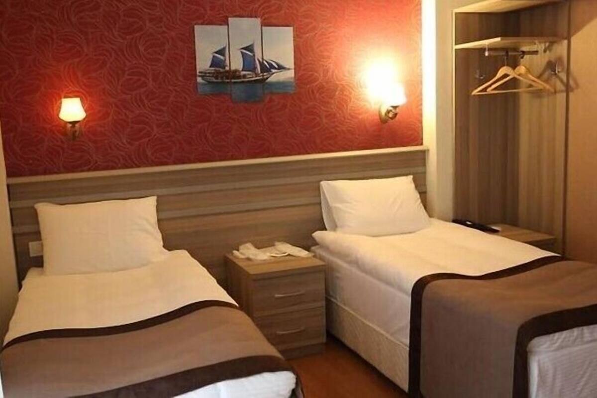Ein Hotelzimmer mit zwei Einzelbetten, einem Nachttisch, einer Wandlampe und einem Kleiderhaken.