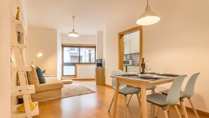 Een modern appartement met een eethoek, een bank en een keuken, zichtbaar door een open deur.