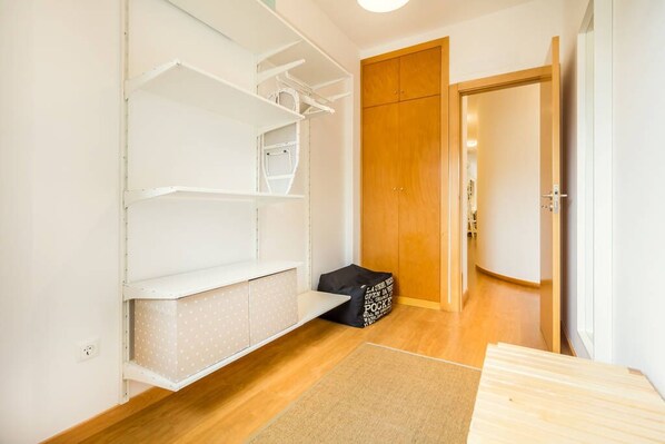 A compact room with a wooden wardrobe, white shelving units, and a small black bag on the floor. - Camões Executive Flat (Porto)
