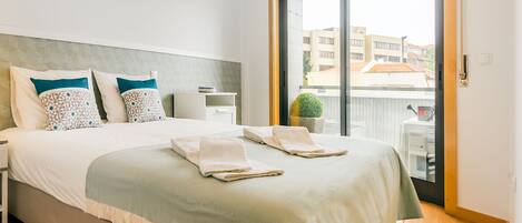 A clean and safe hotel room with a bed, nightstand, lamp, and a view of the city through a large window.