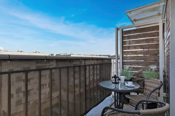 A balcony with a mesh fence, wicker furniture, and a view of the city skyline.