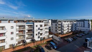 A multi-story residential building with balconies, a parking area, and a clear blue sky.