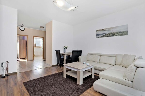 A modern living room with a beige sofa, a wooden coffee table, and a dining area with a table and chairs.
