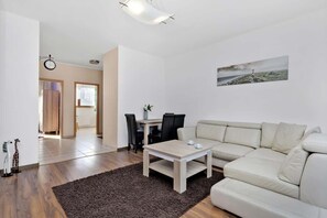 A modern living room with a beige sofa, a wooden coffee table, and a dining area with a table and chairs.