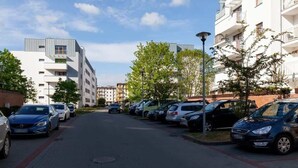 A row of parked cars along a paved street in a residential area with modern buildings and trees.