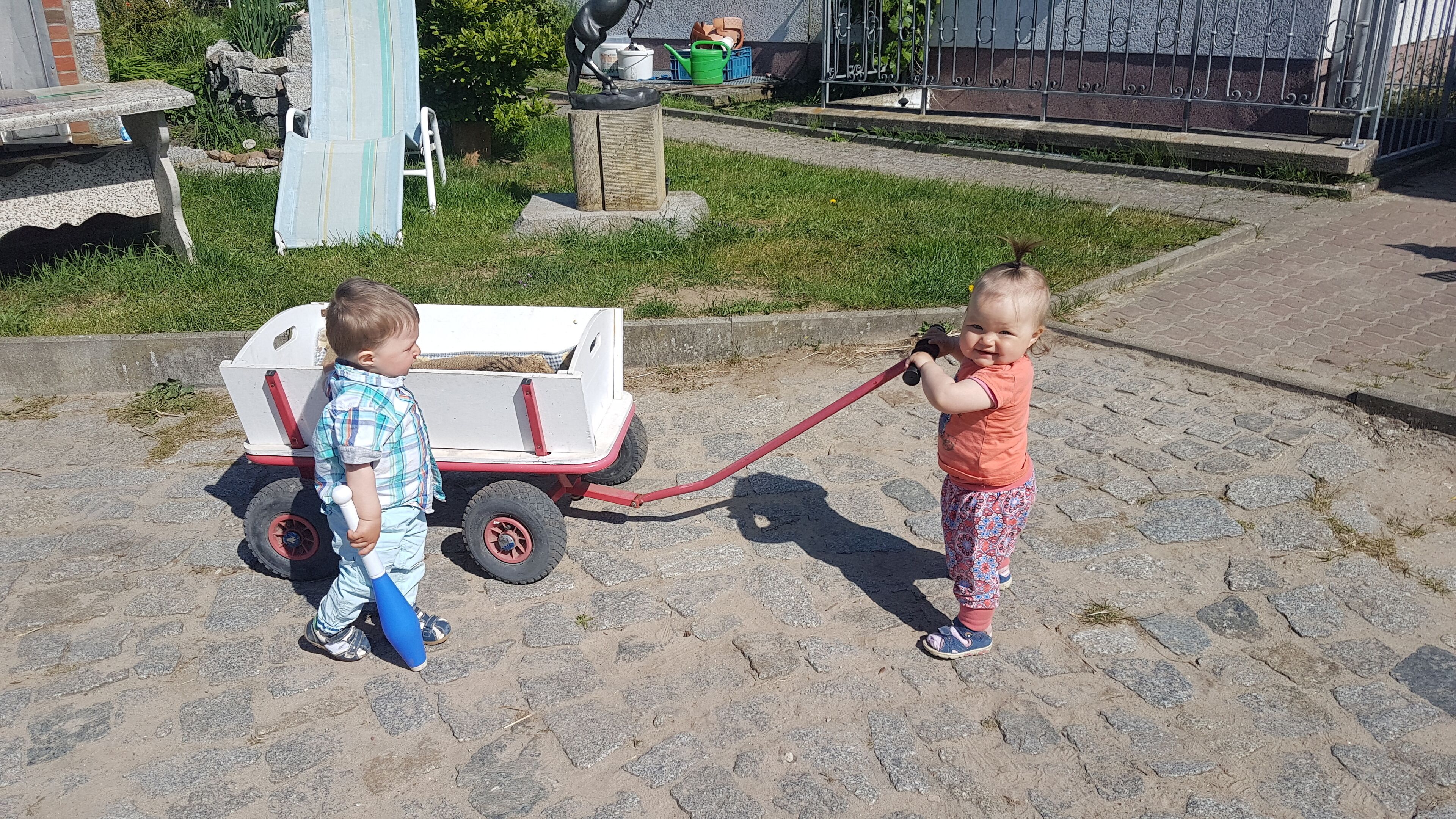 Two children playing with a toy cart on a paved surface.
