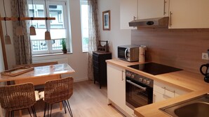 A compact kitchen with a wooden countertop, a built-in oven, a microwave, and a sink. There are wicker chairs and a small dining table. - Apartment with kitchen AND breakfast (Grafenhausen)