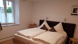 A bedroom with a bed, a nightstand, a window with curtains, and a framed picture on the wall. - Apartment with kitchen AND breakfast (Grafenhausen)
