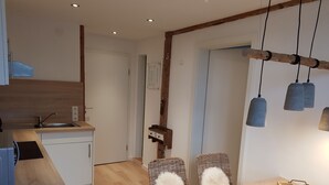 A modern kitchen with a wooden countertop, white cabinets, and a built-in sink. There is a dining area with a wooden table and wicker chairs. - Apartment with kitchen AND breakfast (Grafenhausen)