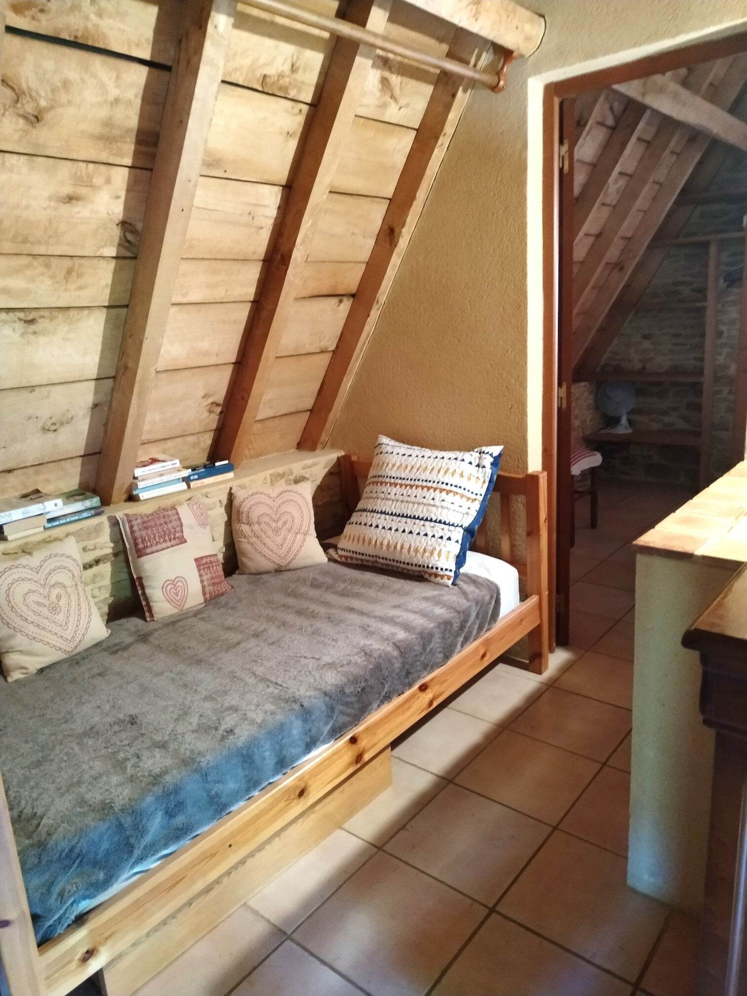 Een slaapkamer in loftstijl met een schuine plafond, houten balken, een bed met een grijze matras en meerdere kussens.