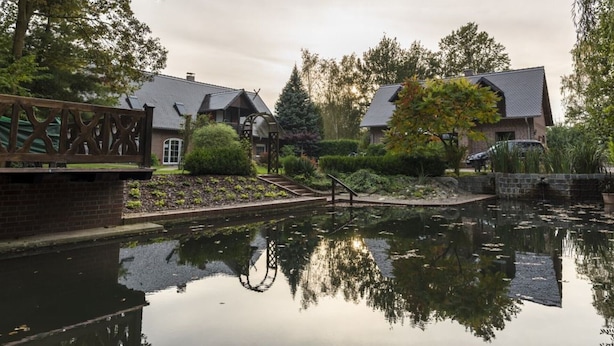 Un patio tranquilo con un estanque que refleja el paisaje, senderos de ladrillo y edificios de estilo tradicional con tejados inclinados.