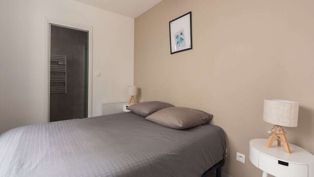 A bedroom with a bed, a bedside table with a lamp, a door, and a framed picture on the wall.