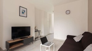 A living room with a flat-screen TV, a laptop on a small table, a brown sofa, and a framed picture on the wall.