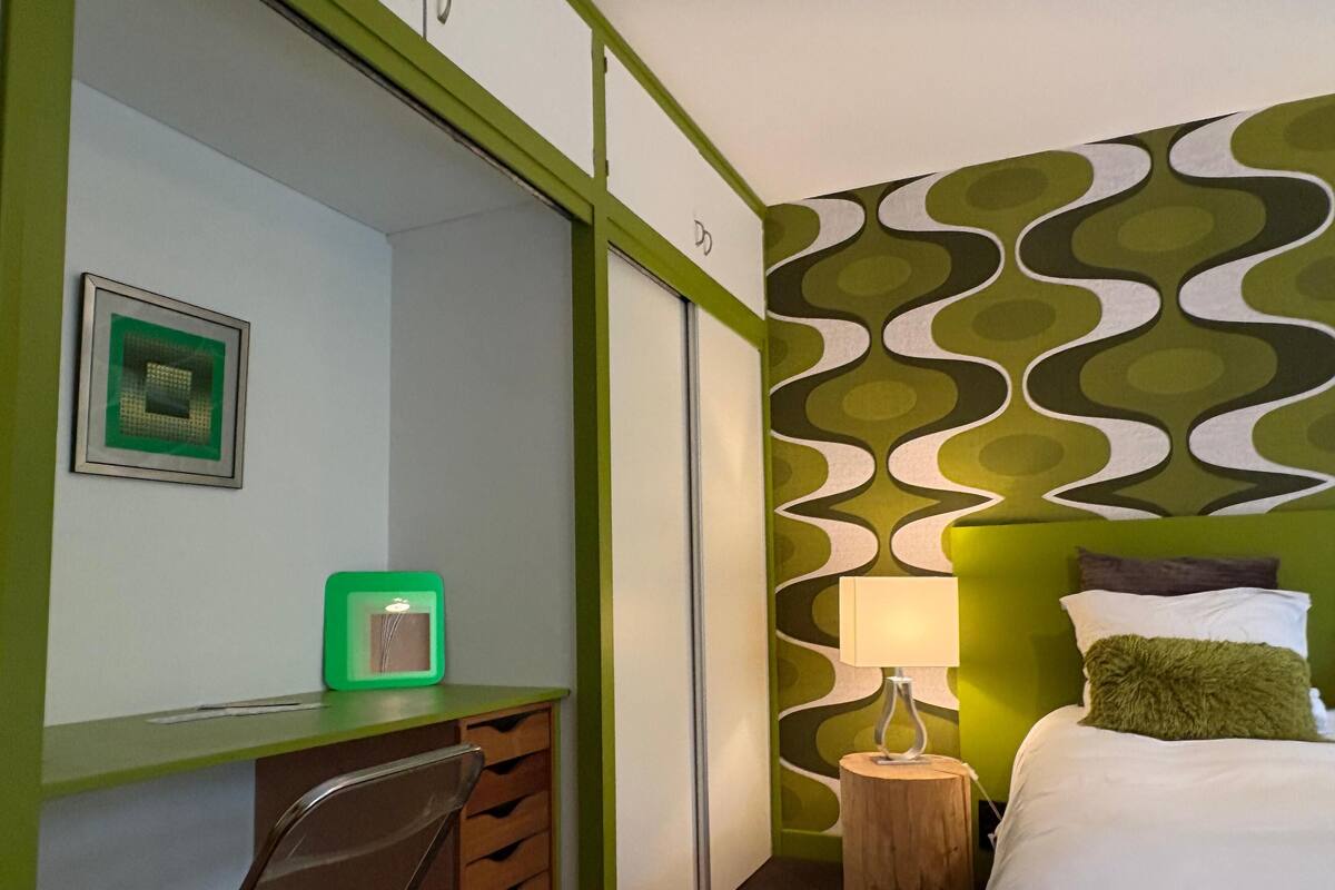 A hotel room with a desk, chair, bed, and a wall with a wavy pattern.