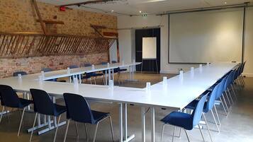 Een vergaderruimte met een lange tafel, blauwe stoelen, een whiteboard en een scherm voor een beamer.