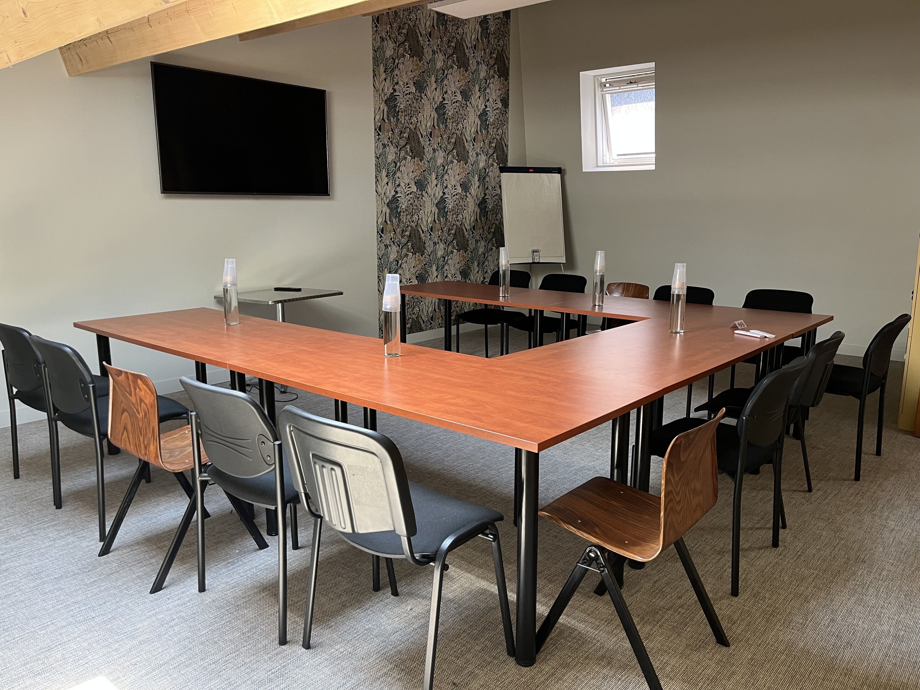 A conference room with a long wooden table, black and brown chairs, a projector screen, and a window.
