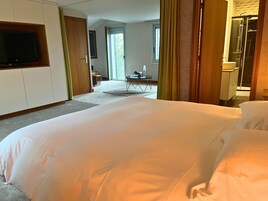Una habitación de hotel con una cama grande, un televisor montado en la pared, una mesita con una silla y un baño visible a través de una puerta abierta.