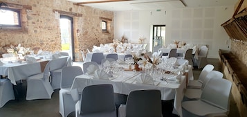 Un comedor con mesas redondas dispuestas para un evento formal, con manteles blancos y sillas, decorado con centros de mesa florales.