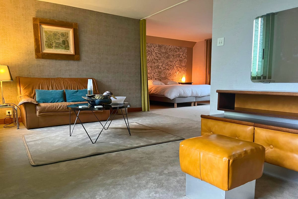 A modern hotel room with a sofa, a coffee table, a TV, and a bed.