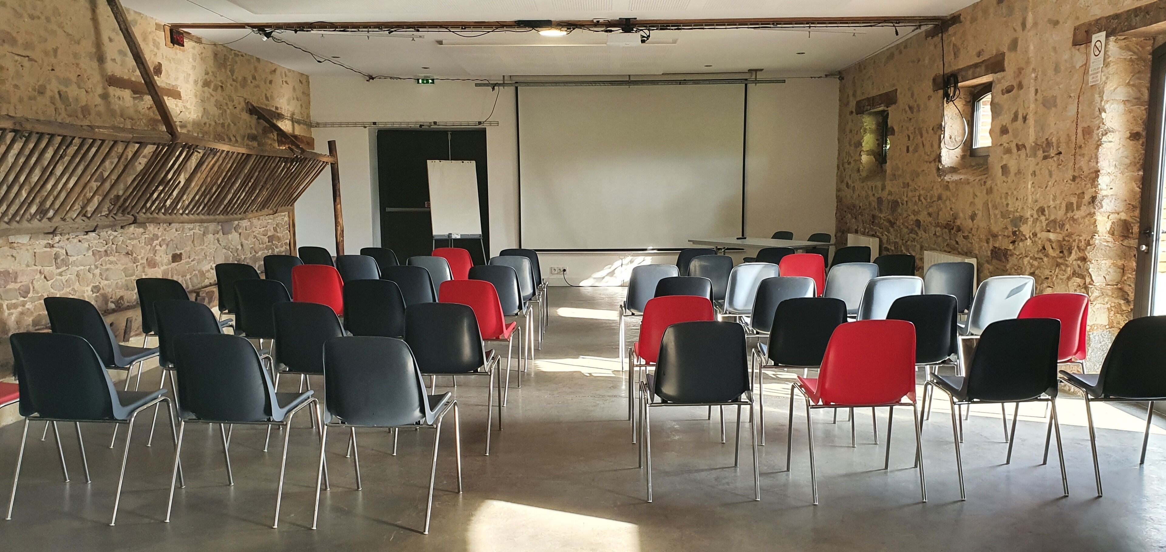 A conference room with rows of chairs, a projector screen, and a stone wall.