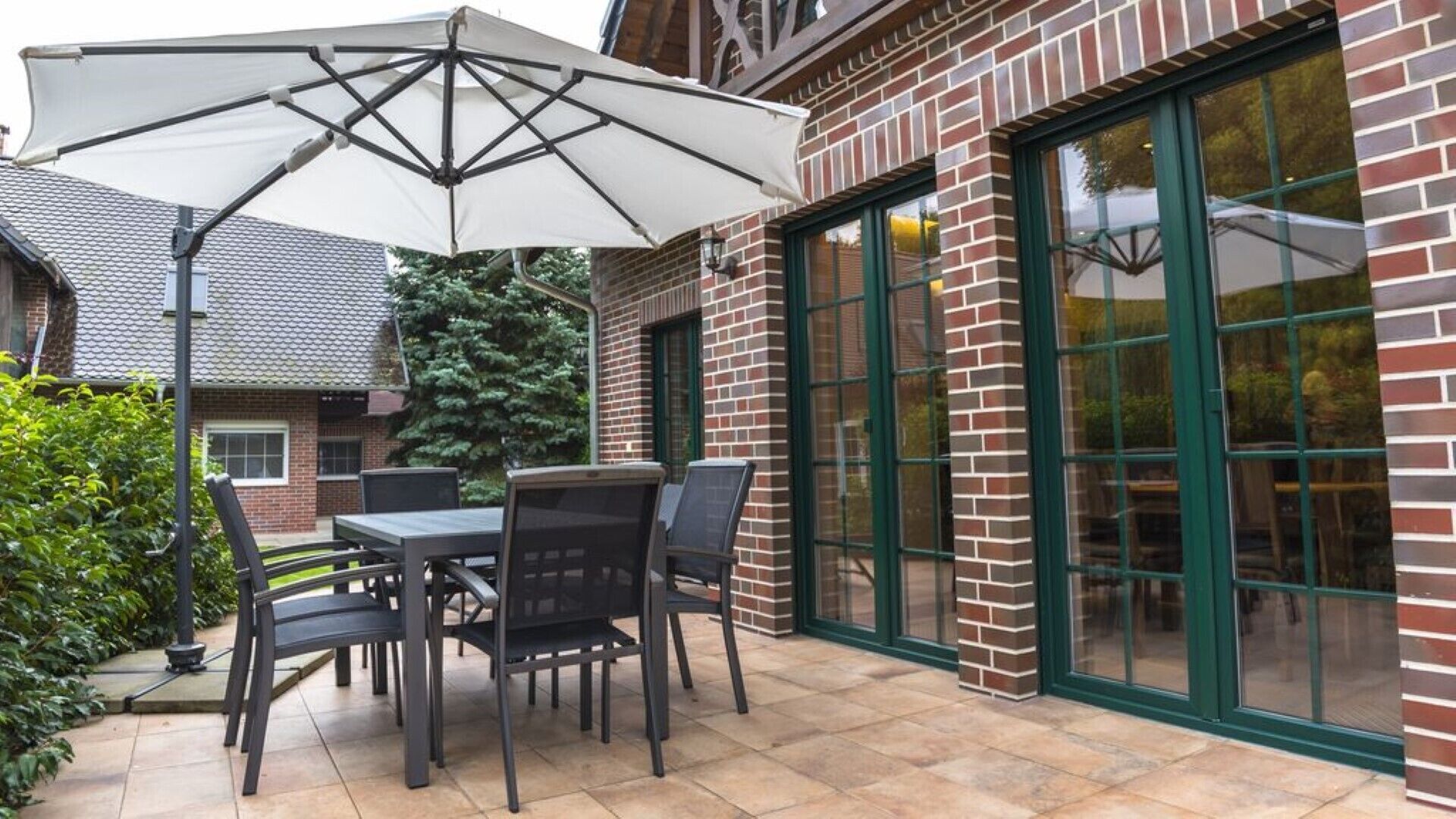A patio with a table and chairs, a large umbrella, and a brick building with a glass door.