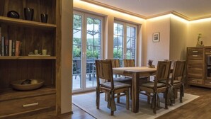 Ein Essbereich mit Holztisch und Stühlen, einem Bücherregal und Blick durch große Fenster.