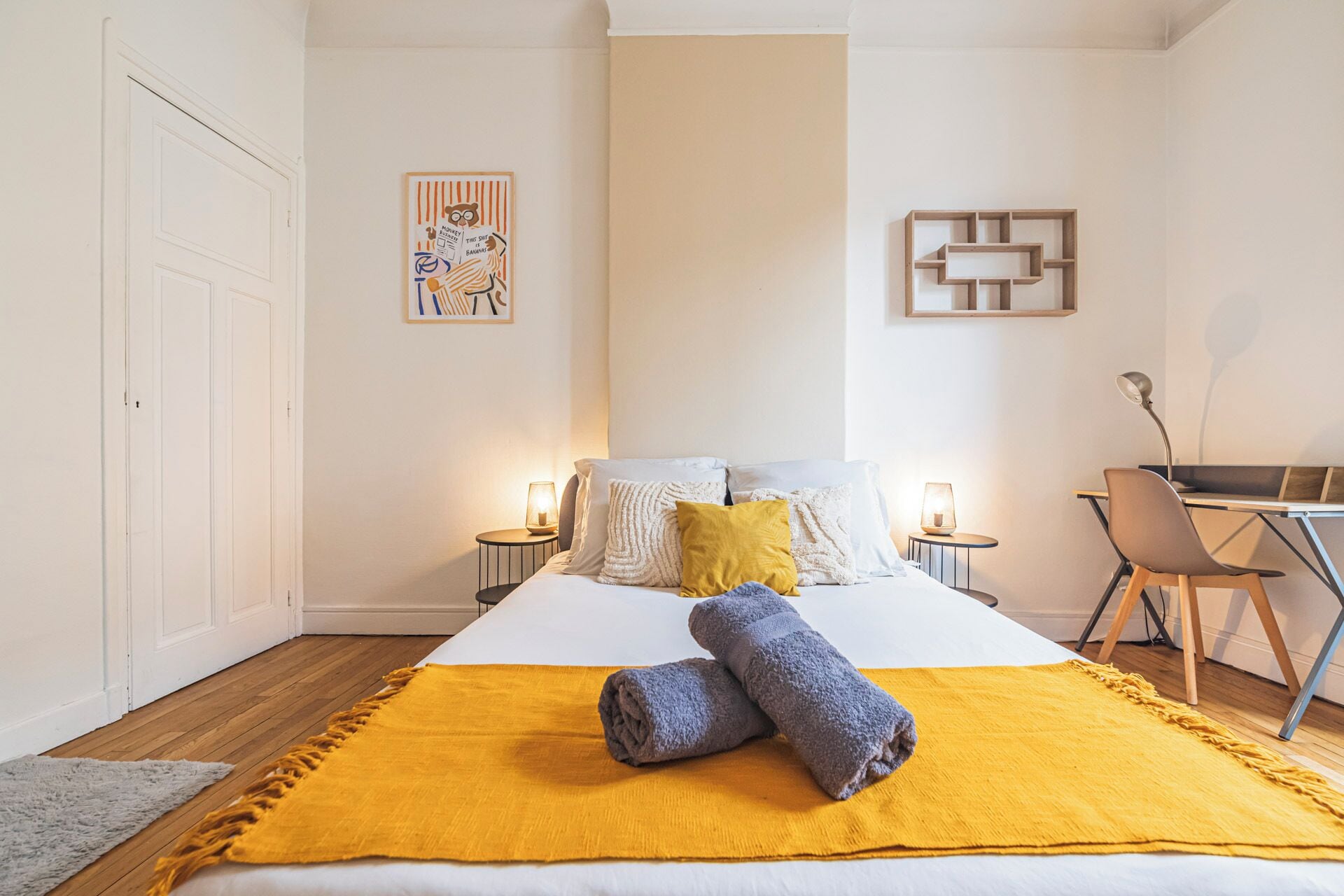 Ein Hotelzimmer mit einem Bett, zwei Nachttischen mit Lampen, einem Schreibtisch, einem Stuhl, einer gelben Tagesdecke und zwei Handtüchern.
