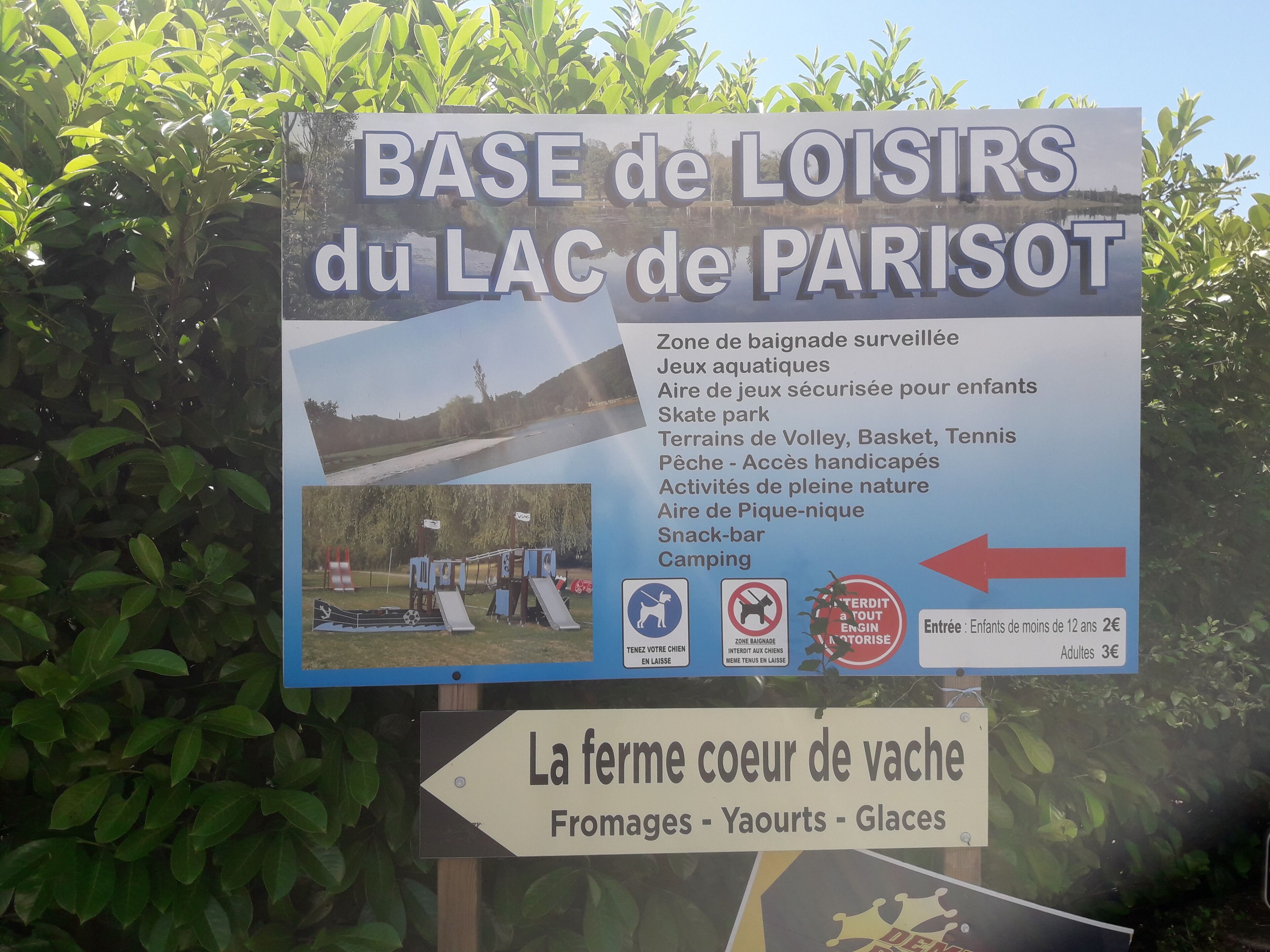 Schild für den BASE de LOISIRS am LAC de PARISOT mit Auflistung von Annehmlichkeiten wie einem überwachten Schwimmbereich, Wasserspielen, einem gesicherten Spielplatz für Kinder, Skatepark, Volleyballfeld, Basketballplatz, Tennisplätzen, Angeln für Menschen mit Behinderung, Naturaktivitäten, einer Snackbar und einem Campingplatz.