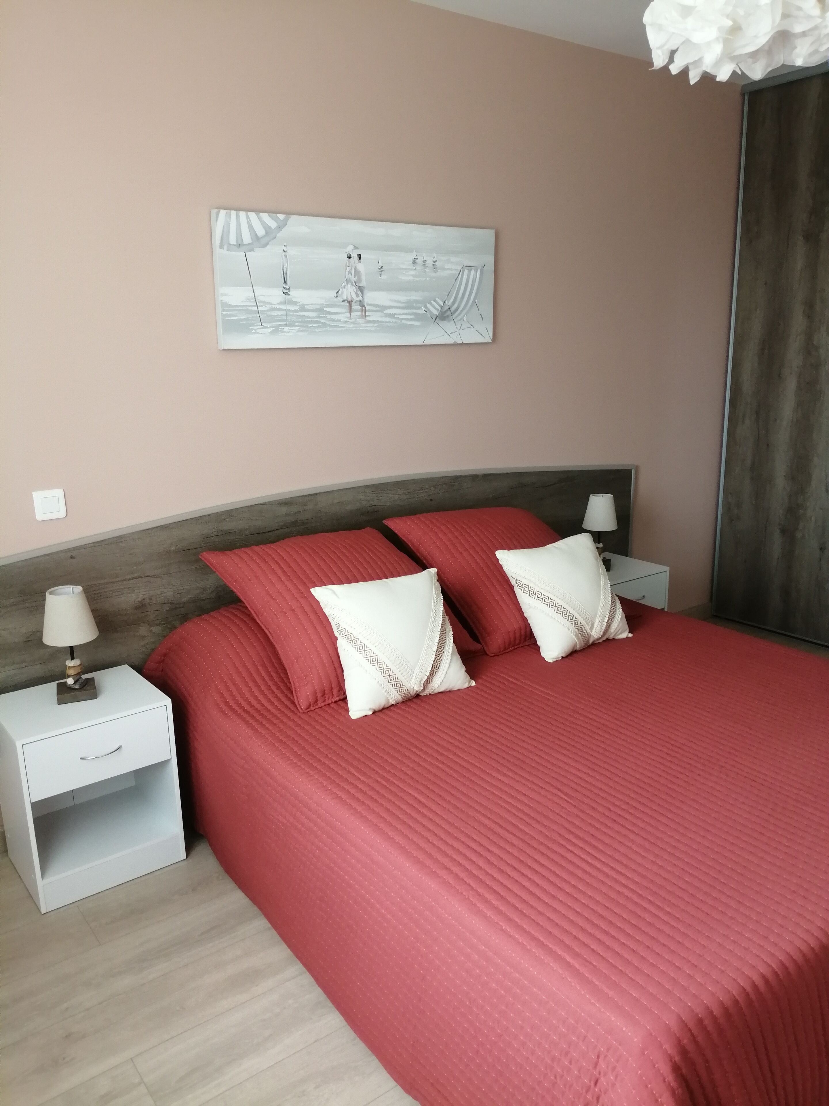 Een slaapkamer met een groot bed, twee nachtkastjes, een lamp en een schilderij aan de muur.
